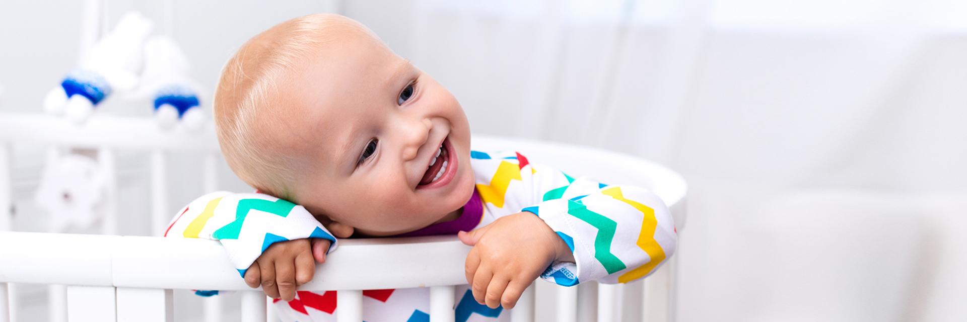 Little boy standing in bed Cute laughing baby standing in bed after nap time. Nursery interior for young kids. Adorable little boy playing in his crib. White furniture for children bedroom.